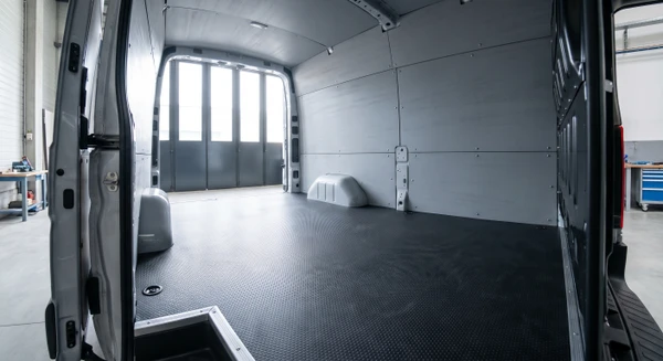 Photographie détaillée de l'intérieur d'un fourgon utilitaire montrant un revêtement de sol professionnel en matériau durable (caoutchouc ou revêtement anti-usure), avec habillage des parois latérales en panneaux de protection ou revêtement robuste. L'image doit mettre en avant les finitions et matériaux des sols et parois, différente d'une vue d'ensemble d'aménagement avec rangements. Plan rapproché ou axonométrique montrant clairement la qualité des revêtements, joints, et protection des surfaces intérieures. Pas de personne présente.