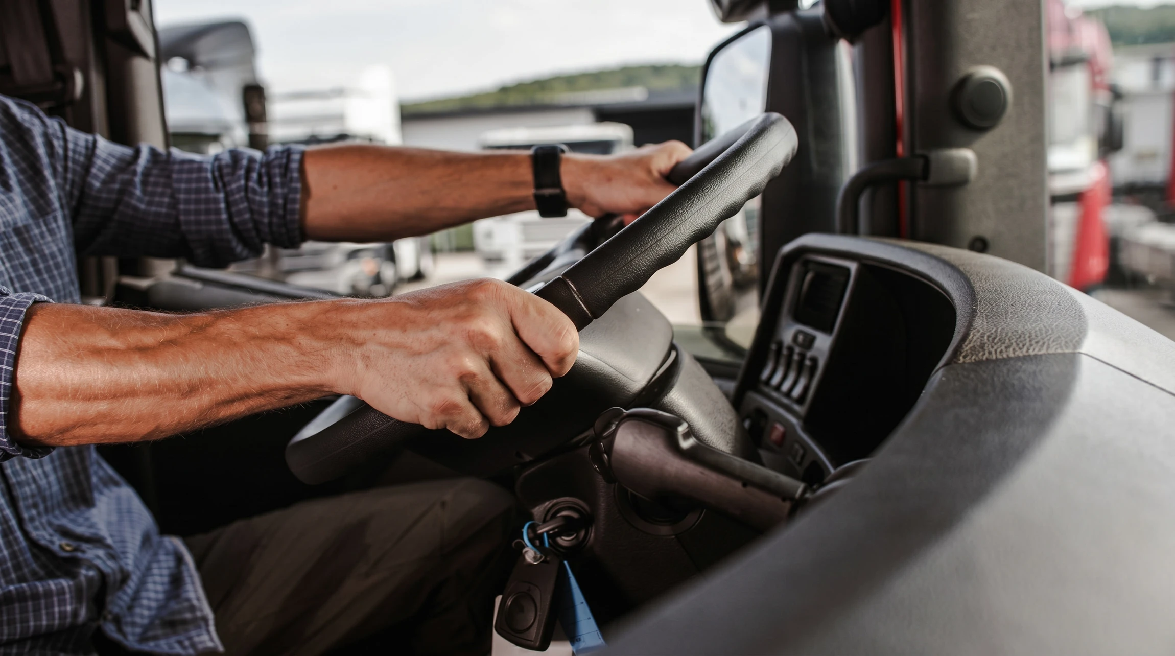 Intérieur d'un véhicule utilitaire avec conducteur en chemise bleue tenant le volant d'une main, contrôlant le levier de vitesses de l'autre